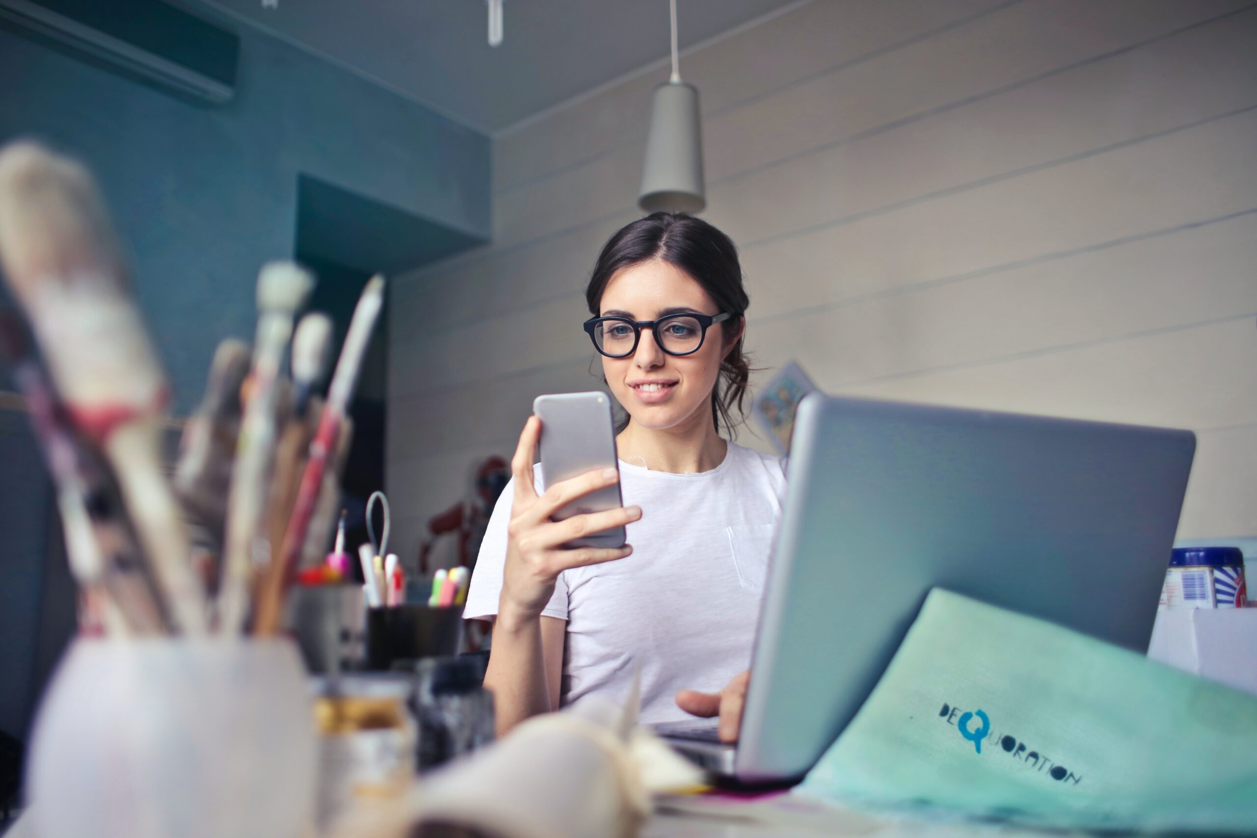 young woman holding a mobile phone in front of laptop