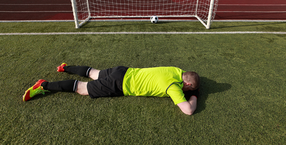 Goal keeper lying face down on a football pitch.