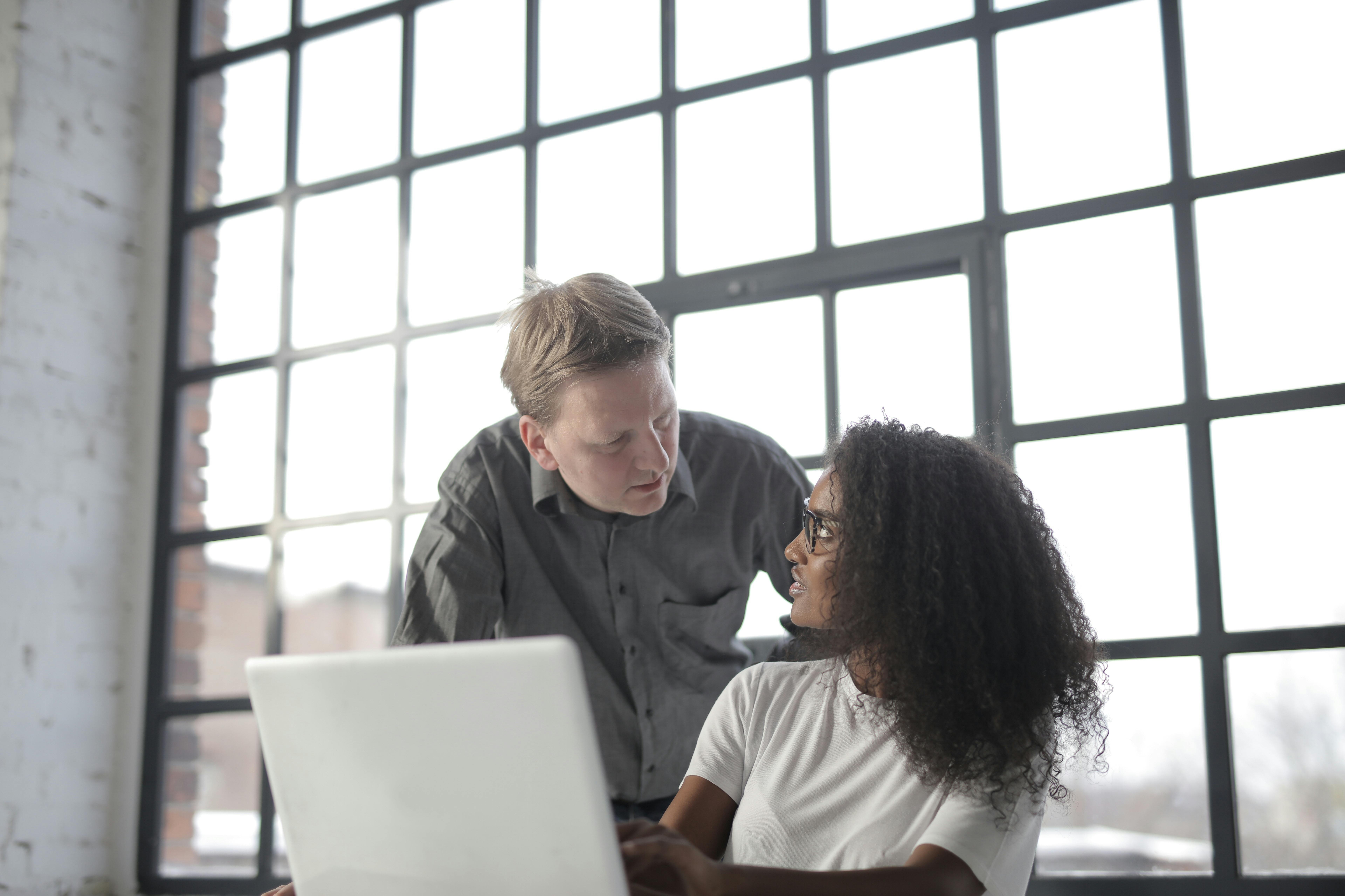 Man leaning over a woman while she's working at a laptop.