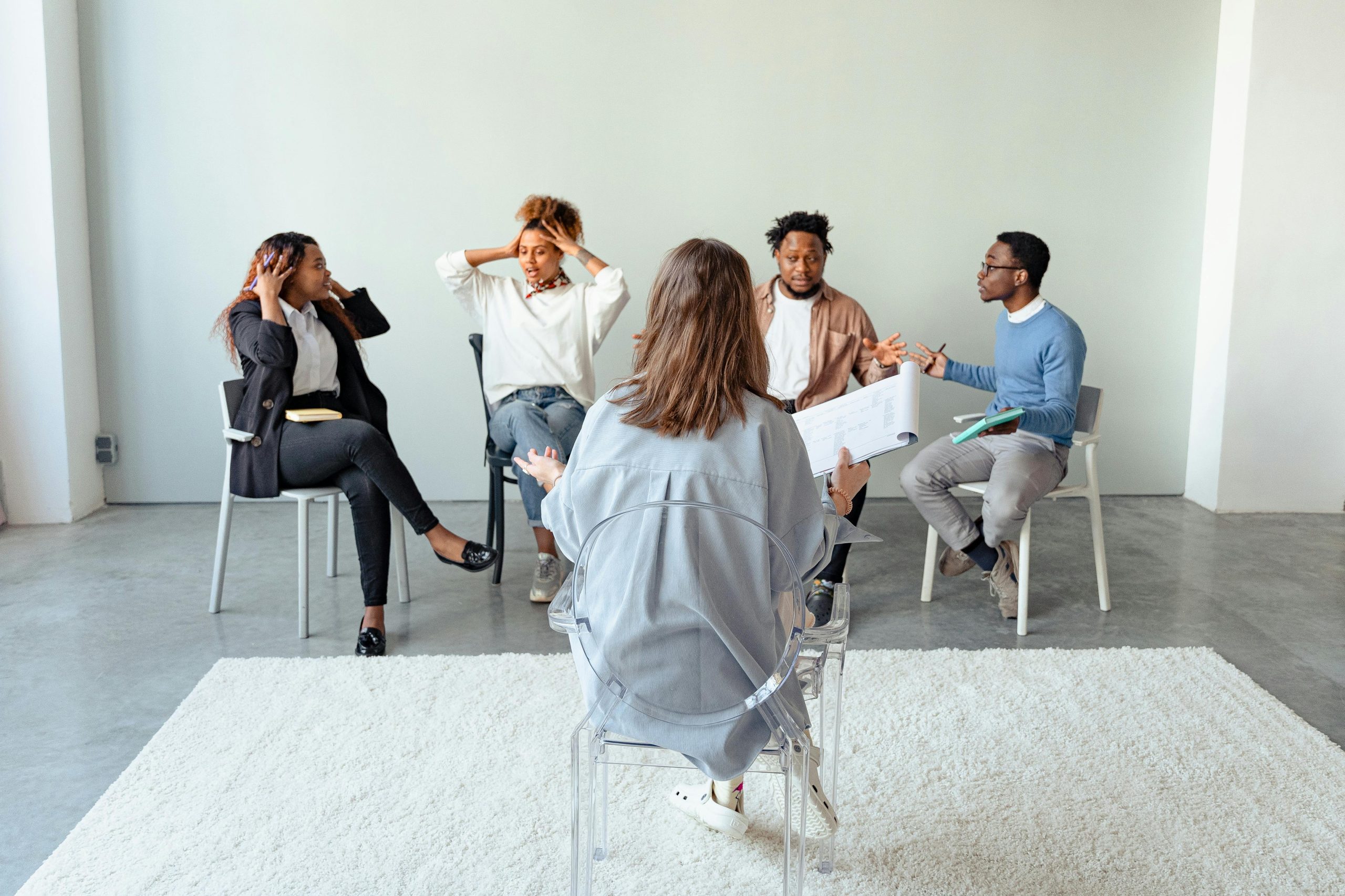 Four people arguing in a room with another trying to mediate.